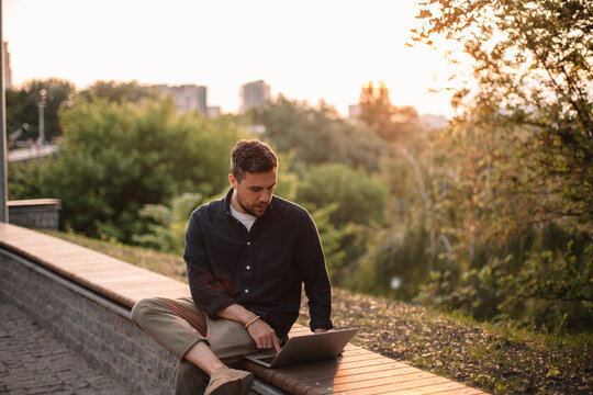 Man using laptop computer sitting on bench in park in summer