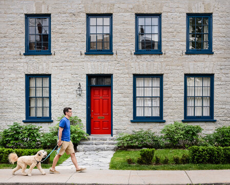 Man walking a dog in front of stone house with red door.