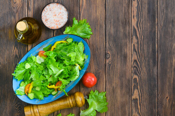 fresh summer green salad with vegetables cucumber, tomato, bell pepper, and leaf lettuce in ceramic bowl, dieting and vegan food on wooden background