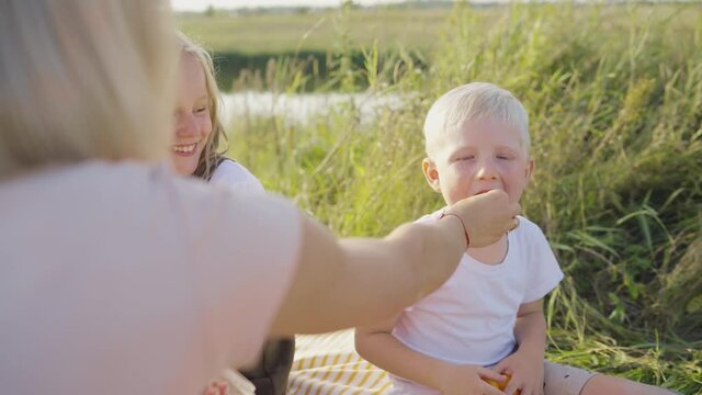 beautiful young mother sits and feeds her son and daughter with raspberries on the green grass close-up. Mom at the picnic feeds the children with raspberries.