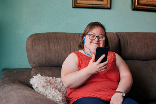 Adult woman with down syndrome smiles and looks her phone at home