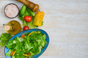 fresh summer green salad with vegetables cucumber, tomato, bell pepper, pink salt and leaf lettuce in ceramic bowl, dieting and vegan food on wooden background with copy space text