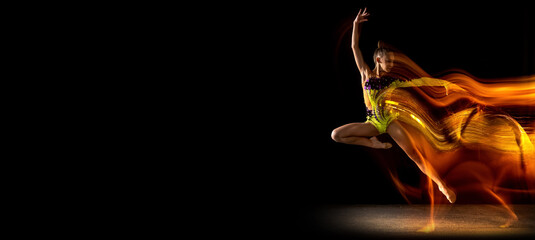 Flyer. Portrait of young girl, rhythmic gymnastics artist in action isolated on dark studio...