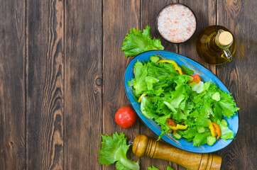 fresh summer green salad with vegetables cucumber, tomato, bell pepper, and leaf lettuce in ceramic bowl, dieting and vegan food on wooden background