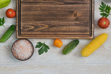 food and culinary background with copy space for text top view, pink himalayan salt and cooking ingredients, fresh vegetables tomatoes, cucumbers, corn  on the kitchen wooden table