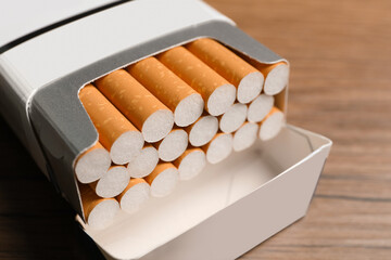 Cigarettes with orange filters in pack on table, closeup