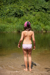 Petite fille en maillot de bain, avec une casquette et les pieds dans l'eau d'une rivière 