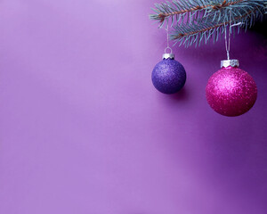 round pink and lilac Christmas shiny balls hang on the branch of the Christmas tree on a light purple background