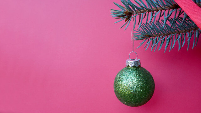 round green Christmas toy ball hangs on the right on a branch of a Christmas tree on a pink background. copy space