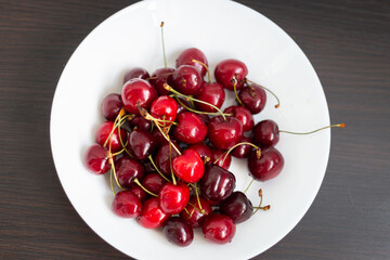 Fresh ripe cherries in a white plate on a dark wooden background. Vegetarian breakfast. Dessert. Healthy eating.