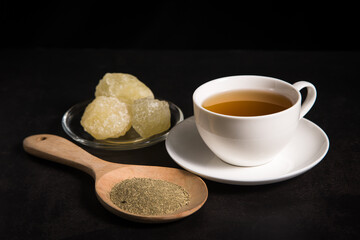 A cup of tea with tea and rock sugar on black tone background.