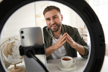 Blogger with cup of tea recording video at home, view through ring lamp