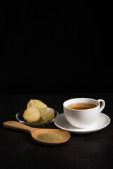 A cup of tea with tea and rock sugar on black tone background.
