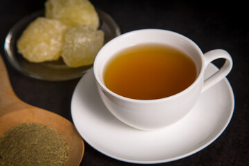 A cup of tea with tea and rock sugar on black tone background.
