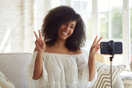 Young mixed-race blogger streaming online in a social network and communicates with her subscribers, recording video vlog podcast on smart phone sitting at home, chatting on a video call