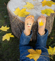 bright yellow autumn maple leaves and a painted smile on the bare feet of a child. joy, cheerful, positive atmosphere, happy childhood. Hello, Autumn. A fun creative idea. autumn fantasies