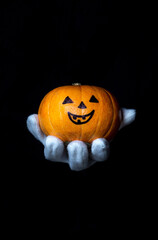 Hand in a white glove holds a pumpkin on a black background