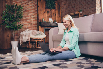 Obraz premium Full length photo of cheerful old happy woman sit floor carpet use laptop smile indoors inside house home