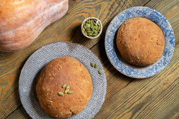 Two rolls of bread with seeds are lying on ceramic plates, next to a fresh pumpkin. Home-made yeast-free dough. Healthy food, top view, flat lay..