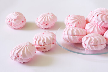 Delicate pink fruit and berry marshmallows along with a transparent plate on a white background