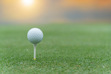 White golf ball on golf pin green grass near hole with golf course background , green tree sun rays