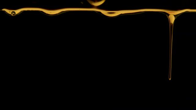 Golden drops of honey drip on a black studio background. The sweet thick liquid drips down. Transparent colorful syrup or oil droplets flowing down. Close up. Slow motion.