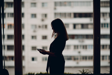 Business woman young adult coach silhouette standing at office window and speaking on mobile phone