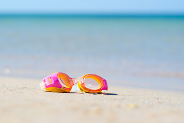 Children's goggles for scuba diving lie on the sandy beach against the background of the sea. Selective focus and shallow depth of field