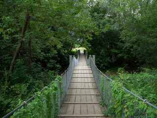 Suspended wooden pedestrian bridge across the river in the middle of the forest.