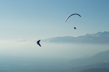 Paraglider and hang glider flying over the mountains in a hazy sky