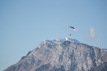 Fototapeta na wymiar Paraglider flying over a white capped mountain in the alps