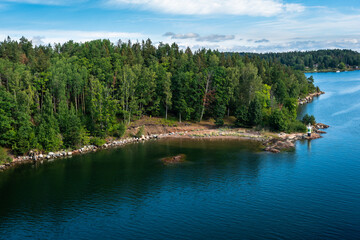 Amazing panoramic view of beautiful evergreens small islands and rocky coast of Scandinavia on summer day. Shot from cruise ship. Skyline. Forest green long coastline. Water voyage to Sweden Stockholm