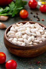 Dry white beans in a wooden bowl on a dark background. Uncooked beans and various ingredients for cooking.