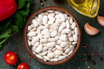 Dry white beans in a wooden bowl on a dark background. Uncooked beans and various ingredients for cooking.