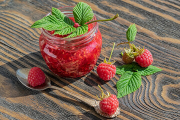 Red ripe raspberries. Homemade raspberry jam in a glass jar on a wooden white table, selective focus, a copy space

