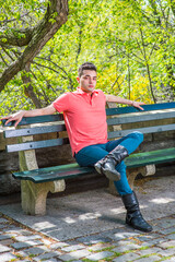 Dressing in a red Polo shirt, green pants and long leather boots, one arm supporting his head, a...