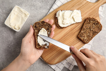 Woman spreading cream cheese onto bread at grey table, closeup