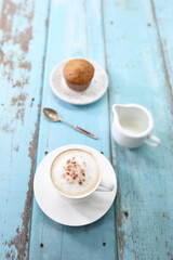 Cappuccino coffee cup and cupcake milk pitcher on blue wooden table