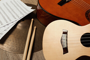 Ukulele, acoustic guitar, drumsticks, cymbal and note sheets on wooden background, closeup. Musical...