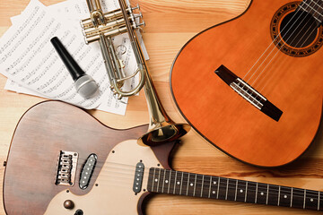 Guitars, trumpet, microphone and note sheets on wooden background, flat lay. Musical instruments