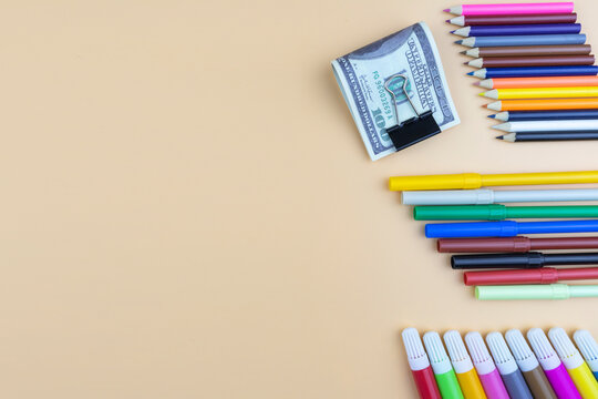 Colorful art supplies and USD 100 dollar bills in a paper clip arranged as a side border on a beige background with copyspace