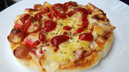 Close-up of small homemade pizza with mozzarella, ham, cheese and tomato sauce. Sprinkle on thick pizza dough. It is served in a round white plate. It is a favorite dish that children can make at home