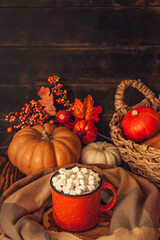 Autumn still life on a wooden background with cocoa mug and marshmallows, checkered scarf, pumpkins, leaves