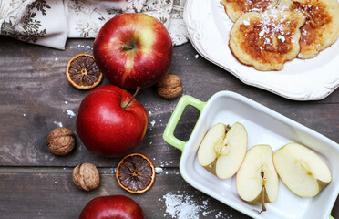 Raw apples and plate with apple fritters on rustic wooden table.