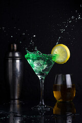 cocktail glasses and yellow and green drink glass with lemon and shaker with black background and liquid flying making a splash