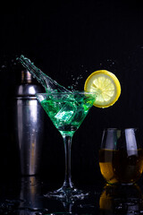 cocktail glasses and yellow and green drink glass with lemon and shaker with black background and liquid flying making a splash