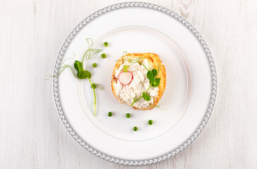 Tasty bread with cream cheese, peas and radish on white plate from above.