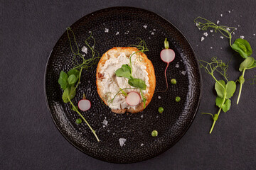 Fototapeta na wymiar Tasty bread with cream cheese, peas and radish on black plate from above.