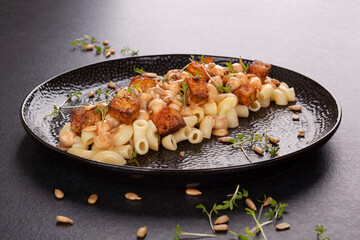 Delicious pasta with chickpeas, fried tofu and fresh herbs on black plate.