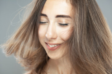 Fototapeta premium Beautiful brunette girl with hair in the air, studio portrait. Happy smiling face expression.